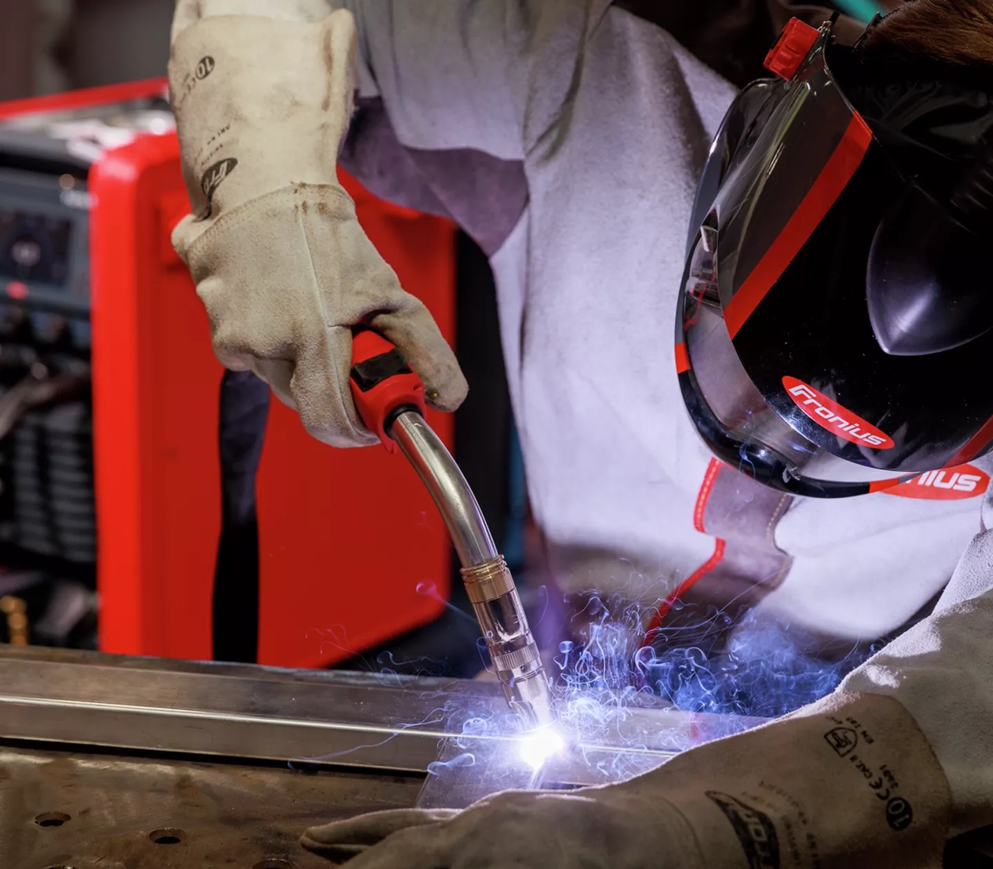 Close-up of a MIG torch welding a steel joint in front of a Fronius welder