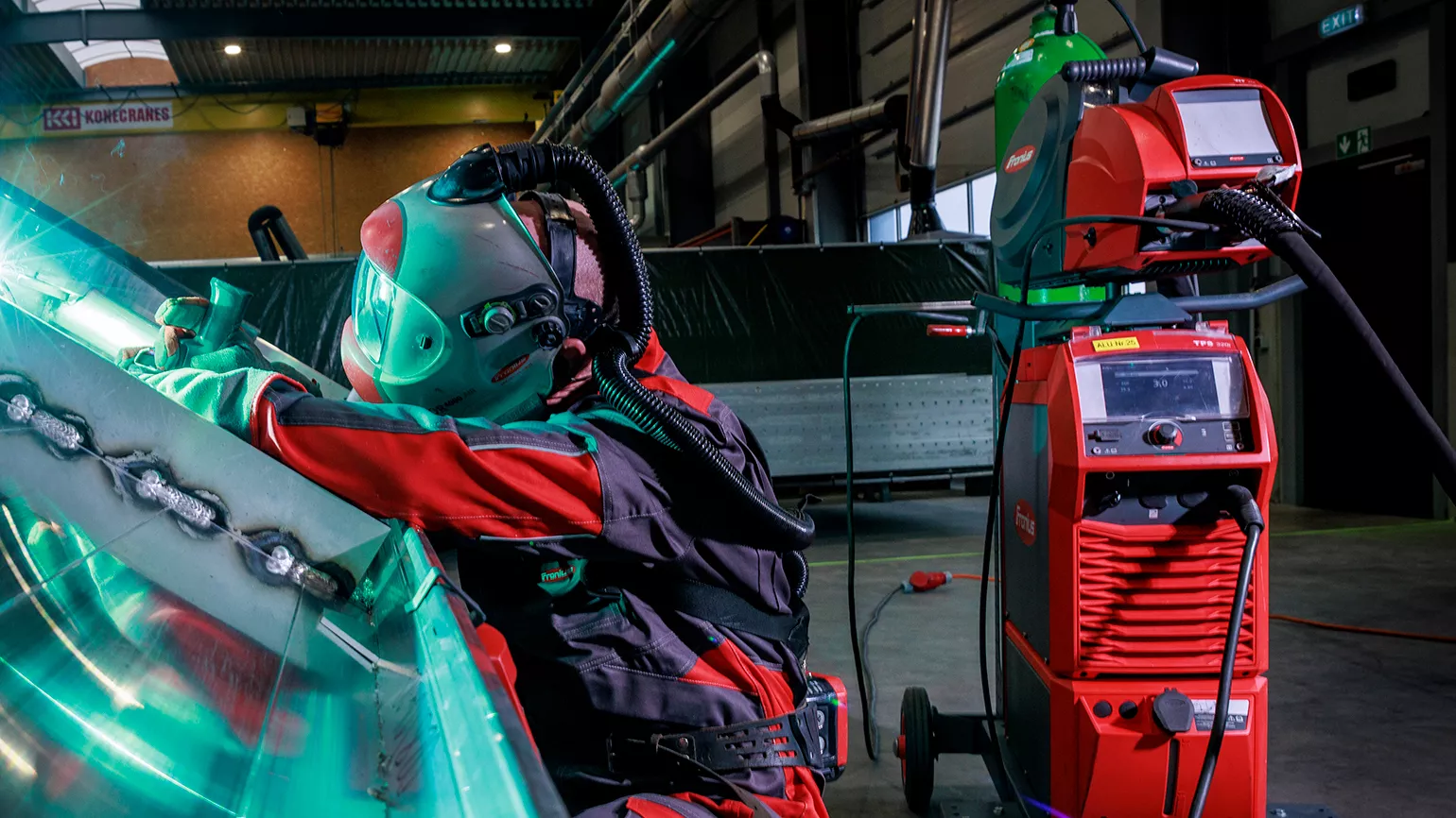 A welder MIG welding sheet metal beside a Fronius TPS/i power source